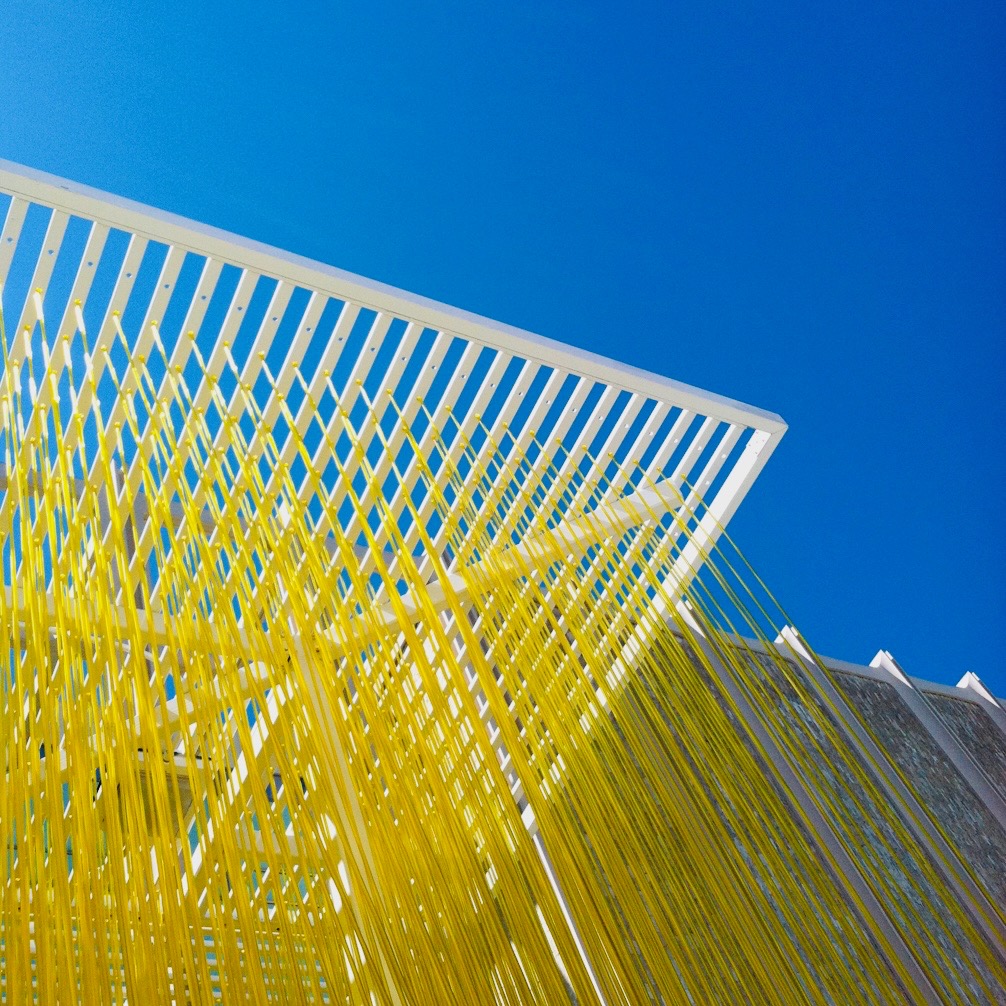 Strands of yellow cord hanging from a white canopy against a deep blue sky